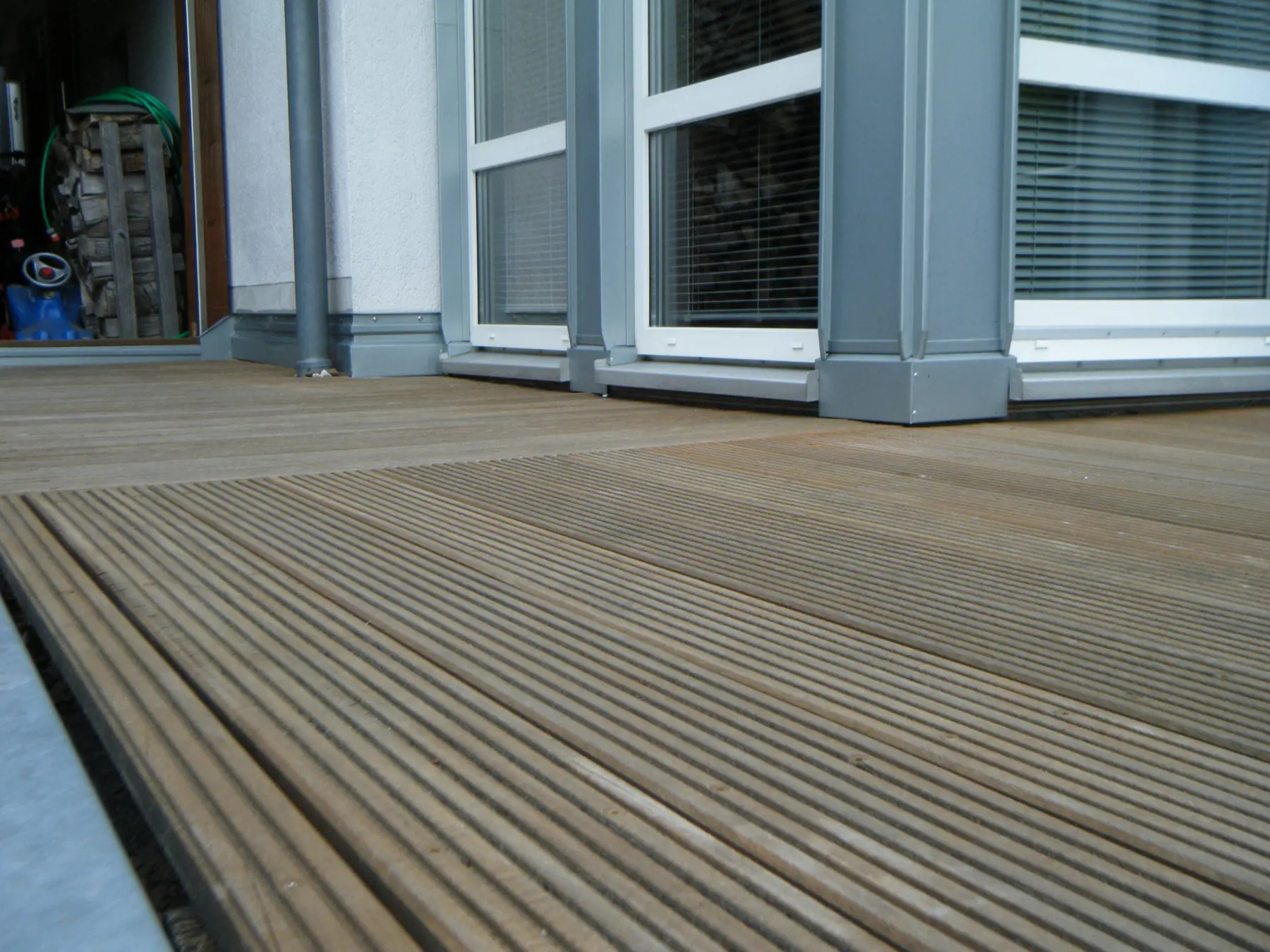 Geriffelte Holzdielen vor einer Fensterfront mit grauen Blechverkleidungen an Pfeilern und Fensterbänken.